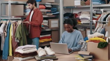Bir dizüstü bilgisayar kullanarak elbise mağazasında çalışan Afro-Amerikalı bir kadın. Bağımsız küçük işletme, depolama kavramı