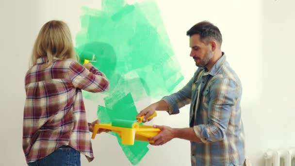 壁のブラシローラーと話と緑の色のアパートで幸せな白人の家族の絵画の壁 夫婦は新しいアパートで修理をしている 国内の活動と人々の概念 — ストック動画