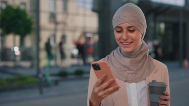 快乐的阿拉伯女商人头戴头巾 带着智能手机在办公中心附近散步 与手握咖啡的朋友们发短信 人员和技术业务概念 — 图库视频影像