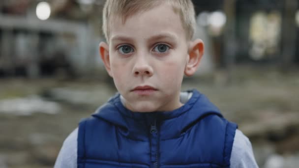 荒廃した背景に子供の肖像画 軍事行動で家を失った悲しい少年がカメラを見ている 子供と戦争だ — ストック動画