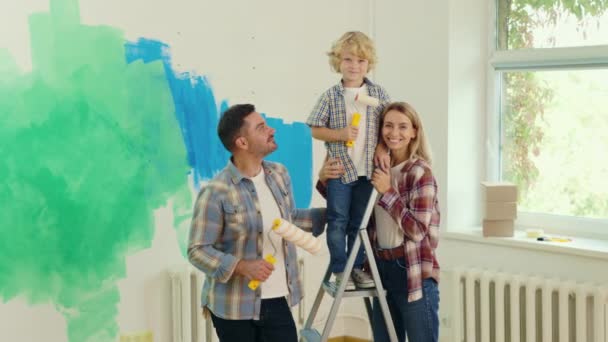 一个快乐的高加索家庭手里拿着油漆滚筒的画像 画室后快乐的年轻家庭 家庭和搬迁 维修概念 — 图库视频影像
