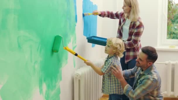 和小男孩在一起的活跃家庭正在粉刷房屋墙壁 整修房间 将墙壁涂成绿色和蓝色 与孩子一起进行大修 丈夫和妻子与小儿子一起做装修 — 图库视频影像