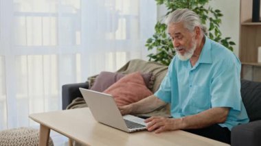 Olgun bir beyaz adam, oturma odasındaki kanepede oturup dizüstü bilgisayarında akrabalarıyla görüntülü konuşma yapıyor. Teknoloji ve insanlar kavramı