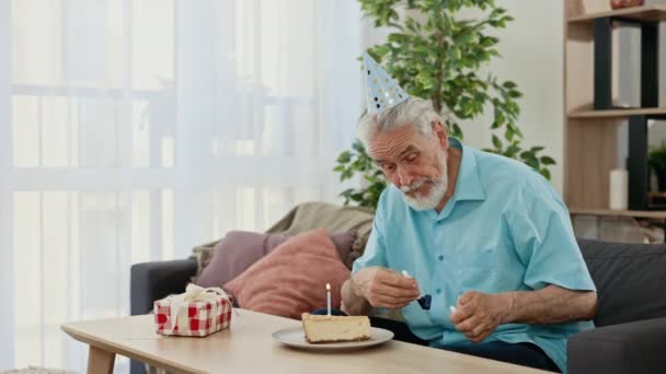 头戴派对帽的垂头丧气的老人坐在桌旁 用燃烧的蜡烛低头看着纸杯蛋糕 生日时感到很不高兴 寂寞的人们庆祝这个概念 — 图库视频影像