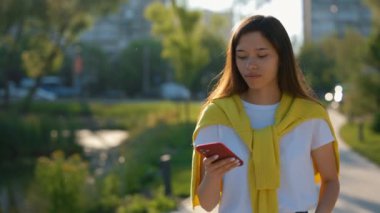 Güzel Asyalı kadın parkta yürüyor, sarı kazak giyiyor, telefon kullanıyor, sesli mesaj kaydediyor. Yürüyüşe çıkmış çekici bir bayan, arkadaşına sesli mesaj kaydediyor.