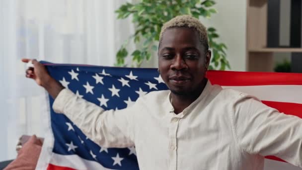 这位快乐的非洲裔美国男性爱国者的画像被套在美国国旗上 坐在客厅沙发上看着摄像机 美国国庆节 — 图库视频影像