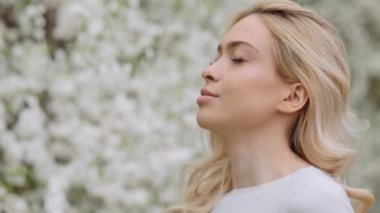 Attractive young lady enjoying enjoys springing garden in bloom. Woman Beautiful Appearance. Relaxed beautiful caucasian female spending free time on the blooming sakura trees background