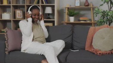 Happy pregnant african american woman putting wireless earphones on her pregnant belly, enjoying favorite music with baby. Concept of love, care and maternity