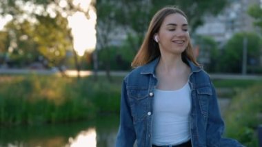 Happy smiled caucasian woman listening to music from the earphones, holding smartphone, dancing while walking outside. Beautiful young lady dancing while listening to music
