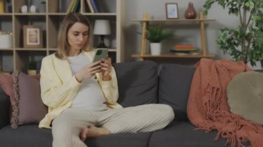 Pregnant caucasian woman feeling labor contractions while searching information about babies on smartphone. Concept of maternity and technology.