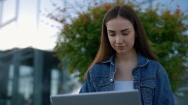 Caucasian female student with laptop outdoors. Young woman using laptop for preparing for exams. Technology, education and remote working concept