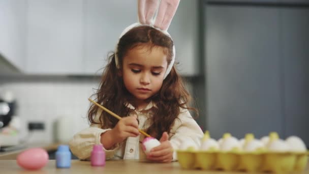 小さな女の子は 伝統的な春の夕食のためにピンクの塗料で卵をペイント ハッピーイースター 子供は家でイースターの装飾を作ります かわいい子供は休日の準備のために東部の日にウサギの耳を身に着けています — ストック動画