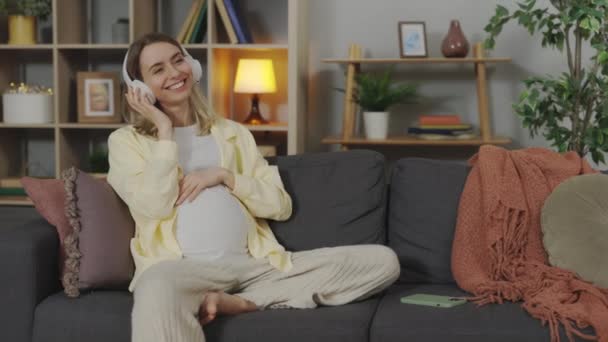 Happy Pregnant Woman Sitting Comfy Sofa Putting Wireless Headphones Her — Vídeo de Stock