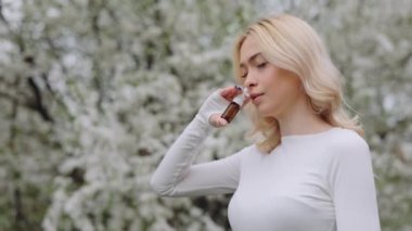 Sick dissatisfied woman spraying nasal medicine during walk in flowering spring garden. Antiallergic and symptomatic treatment of rhinitis. Side view