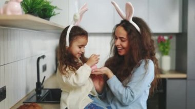 Mutlu Paskalyalar. Tavşan kulaklı anne ve kızı Paskalyayı kutluyor ve evde boyalı yumurtalarla oynuyorlar. Paskalya tavşanı. Yumurtaları boyama geleneği. Mutlu aile Paskalya için hazırlanıyor.