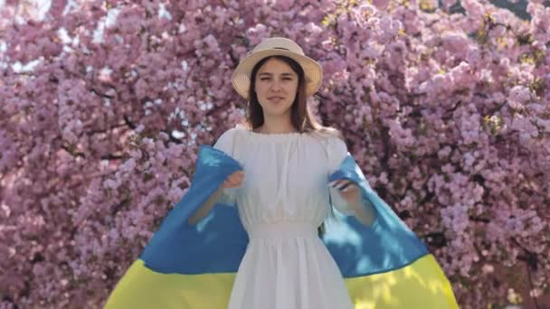 Glimlachende Jonge Vrouw Omhelst Trots Oekraïense Vlag Terwijl Bloeiende Tuin — Stockvideo