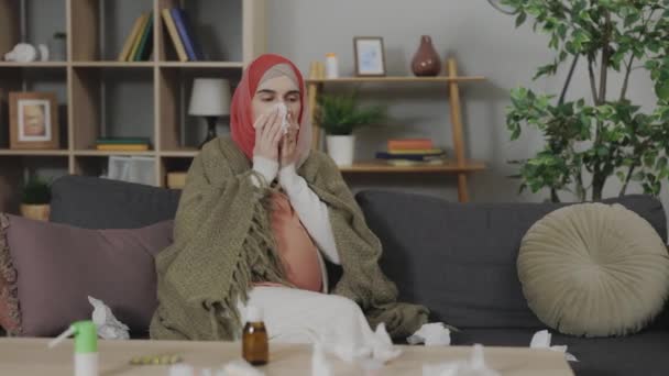 阿拉伯孕妇裹着毛毯 在家里得了流感 流鼻涕 病女坐在客厅沙发上 头戴头巾 把鼻子吹进纸巾里 — 图库视频影像
