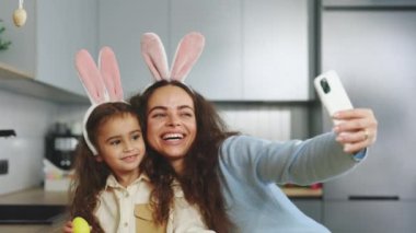 Smiling Mother and Daughter Selfie with Easter Eggs, Wearing Bunny Ears, Beauty and Fun Day Together at Home. Happy Easter. Concept of Childhood, Technology, Familys Weekend