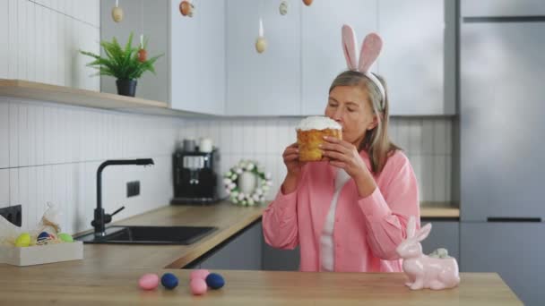Eine Ältere Frau Mit Hasenohren Sitzt Küchentisch Und Isst Osterkuchen — Stockvideo