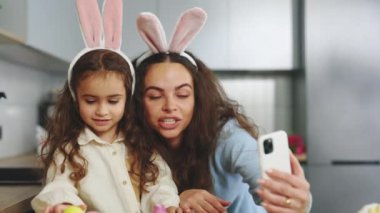 A Happy Family Is Preparing for the Easter Holiday Using Smartphone to Video Calling. Mom and Daughter Paint Eggs, Communicate With Friends Through Video. Happy Easter