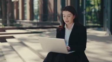 Smiled Business Woman in Formal Suit Sitting on the Business Centre Stairs Working on Laptop for Working Purposes. People and Technology Concept