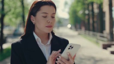 İş Dünyası Kadını Giyinik vaziyette İş Merkezi 'nin yanında duruyor. Cep telefonunu kullanıyor, müşterilerle mesajlaşıyor, uygulamaları yürütüyor. Yakın çekim. Halk ve Teknoloji Konsepti