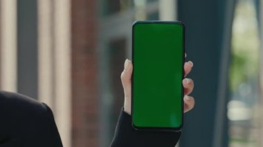 Close-Up Shot of Green Screen Template Smartphone in Female Hands at Street. Woman Using Phone with Green Mock-Up Screen Chroma Key. Technology and Green Screen Concept