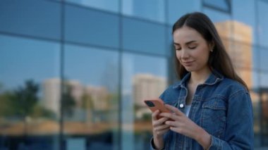 Business Woman Standing Near the Business Centre, Using Smartphone for Working Purposes, Working on the Phone. Caucasian IT Worker Working Near the Business Centre. People and Technology Concept