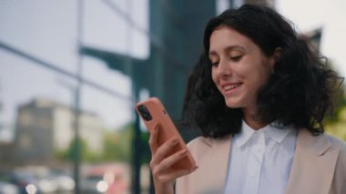 Çok Etnik Kıvırcık Gülümseyen Güzel İş Kadını Akıllı Telefon kullanarak İş Merkezinin Yakınındaki Resmi Kıyafet Duruşunda. Yakın çekim. Halk ve Teknoloji İş Konsepti