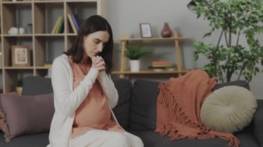 Caucasian Pregnant Woman Experiencing Maternity Depression and Struggling With Hormonal Changes. Worried Lady Sitting on Sofa in Modern Living Room, Deep in Thought About Health Issues