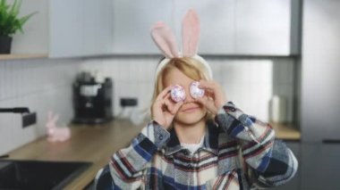 Happy Easter. Portrait of a Happy Little Boy Wearing Bunny Ears and Holding a Colorful Easter Egg in Front of His Eye, Having Fun at the Camera. Preparation for the Holiday Concept
