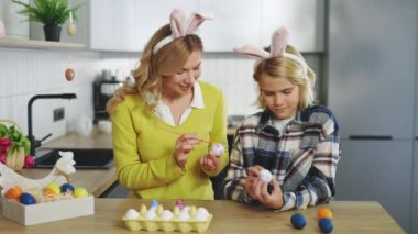 Happy Easter. Caucasian Mother and Son in Rabbit Ears Son Draw on Painted Eggs at the Table, at Home. Funny Family Prepares for Easter Holiday