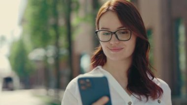 Ginger Business Woman wearing Formal Suit Standing near the Office Centre using the Mobile Phone, Texting with Clients, Swiping Apps. Close up. People and Technology Concept