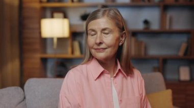Portrait of Beautiful Smiling Old Lady Portrait Looking in Camera Sitting in the Living Room at Home. Calm Old Lady Looking at Camera at Home Interior. Elderly Senior Female Relaxed on the Couch