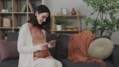 Kafkasyalı kadın rahat koltukta otururken ultrason taraması yapıyor ve karnına dokunuyor. Evde Doğmamış Bebeğin İlk Sonogram Görüntüsüyle Genç Bayan Geleceğin Anneliğinin Zevkini Çıkartıyor