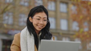 Attractive Asian Girl Sitting Outside on the Bench, Working on Laptop. Young Teacher is Working Out in the Park. Foreign Female Student is Studying Using Computer Near Campus. Close Up