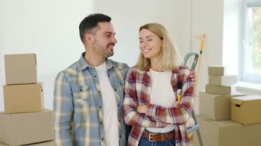 Portrait of the Happy Couple Who Makes Repairs in a New House. Smiling Family Standing in Their Apartment with Paint Brush in Hand. Relocation, Moving and Repair Concept