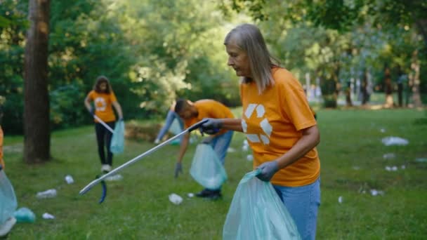 在收集垃圾袋中的垃圾时 使用垃圾捡拾机对成熟的生态志愿者进行微笑 环保人士团体身穿环保T恤清洁公园 人民拯救环境 生态概念 — 图库视频影像