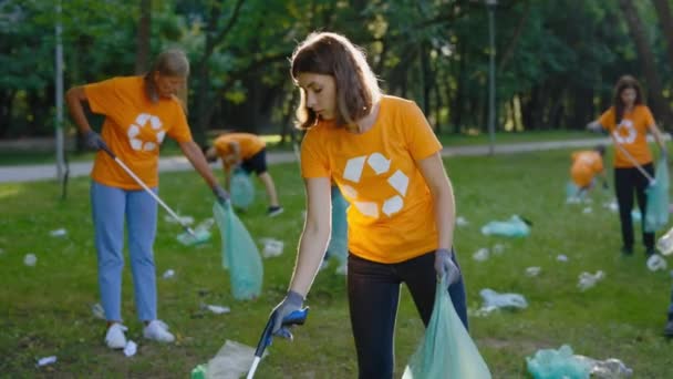 在收集垃圾袋中的垃圾时使用垃圾捡拾器的妇女生态志愿者 环抱符号清洁公园的T恤环保人士团体 生态概念 循环再用 — 图库视频影像