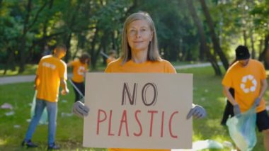 Kirli Orman Arkaplanında Plastiksiz Poster Tutan Kıdemli Kadın Eylemci Dışarıda Duruyor. Halka açık bir gösteri. Çevre aktivistleri, arka plandaki çöplükten Park 'ı temizliyor