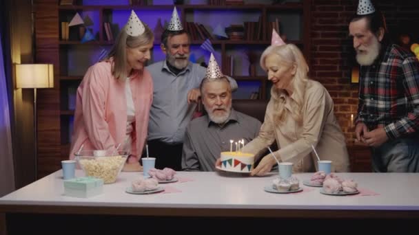 有生日聚会的老年人小组 和他的朋友一起在养老院庆祝 穿着派对帽的老人坐在餐桌前 在蛋糕上吹蜡烛 成熟的乐趣 — 图库视频影像