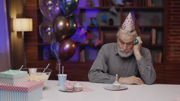 Депрессивный Пожилой Человек Шляпе Вечеринок Сидит Столом Дома Смотрит Вниз — стоковое видео
