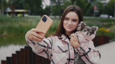 Çekici Gülümseyen Kafkas Kadın, sevimli küçük Chihuahua 'sıyla duruyor ve köpeğiyle selfie çekiyor. Teknoloji, Köpekler Dostluk Konsepti