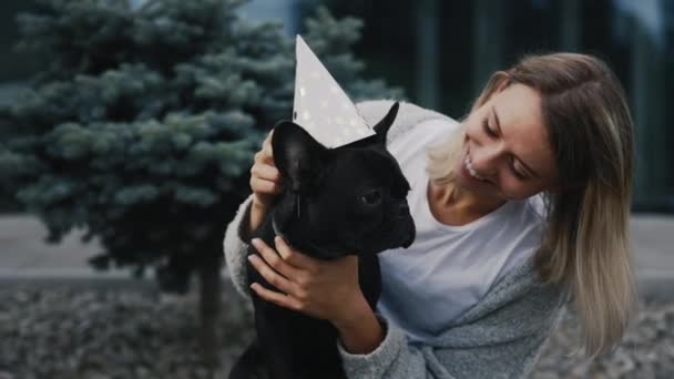 ペットの誕生日を祝う 幸せな白人女性彼女のフランスのブルドッグの誕生日を祝う彼に誕生日の帽子をかぶって 幸せな気分 人と犬の友情の概念 — ストック動画