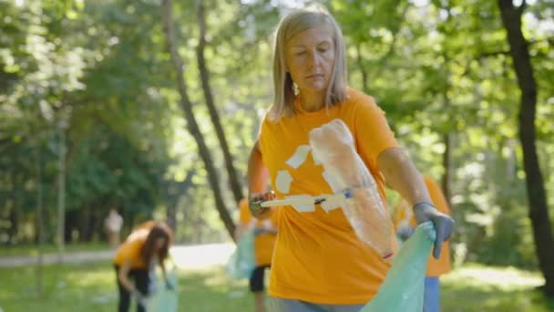 白种人老年女性环保义工在收集垃圾袋中的塑料时使用垃圾捡拾器 环抱符号清洁公园的T恤环保人士团体 安全生态概念 — 图库视频影像