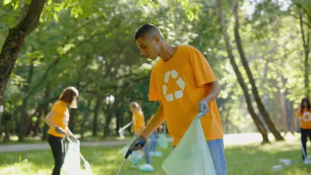 在收集垃圾袋垃圾时 多种族人士使用垃圾箱 不同的志愿者团体在T恤回收符号清洁公园 安全生态概念 — 图库视频影像