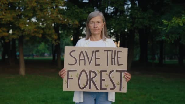 拯救森林海报 高级女权运动者在森林中持有生态海报 并看着相机 公众示威 自然卫士 生态学 绿色地球 — 图库视频影像