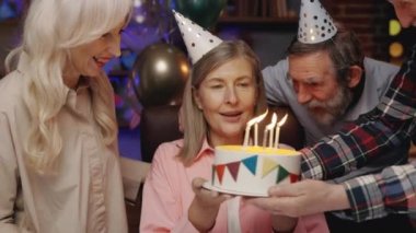 Doğum günü pastasında mumları üfleyen yaşlı bayan huzurevindeki diğer yaşlılarla birlikte kutluyor. Doğum günü partisi, Eski Dostlar Üflüyor Parti Kornaları