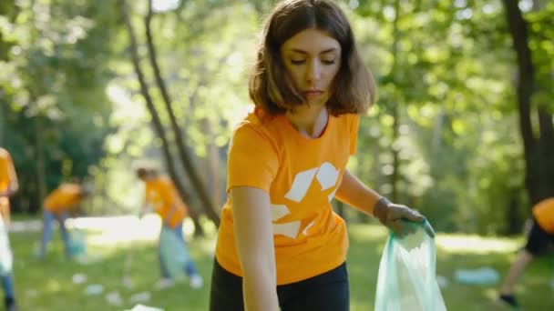 白种人女性环保义工在收集垃圾袋中的塑料时 使用垃圾捡拾器 环抱符号清洁公园的T恤环保人士团体 安全生态概念 — 图库视频影像