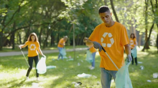 多种族年轻人在收集垃圾袋中的垃圾时使用垃圾捡拾器 不同的志愿者团体在T恤回收符号清洁公园 安全生态概念 — 图库视频影像